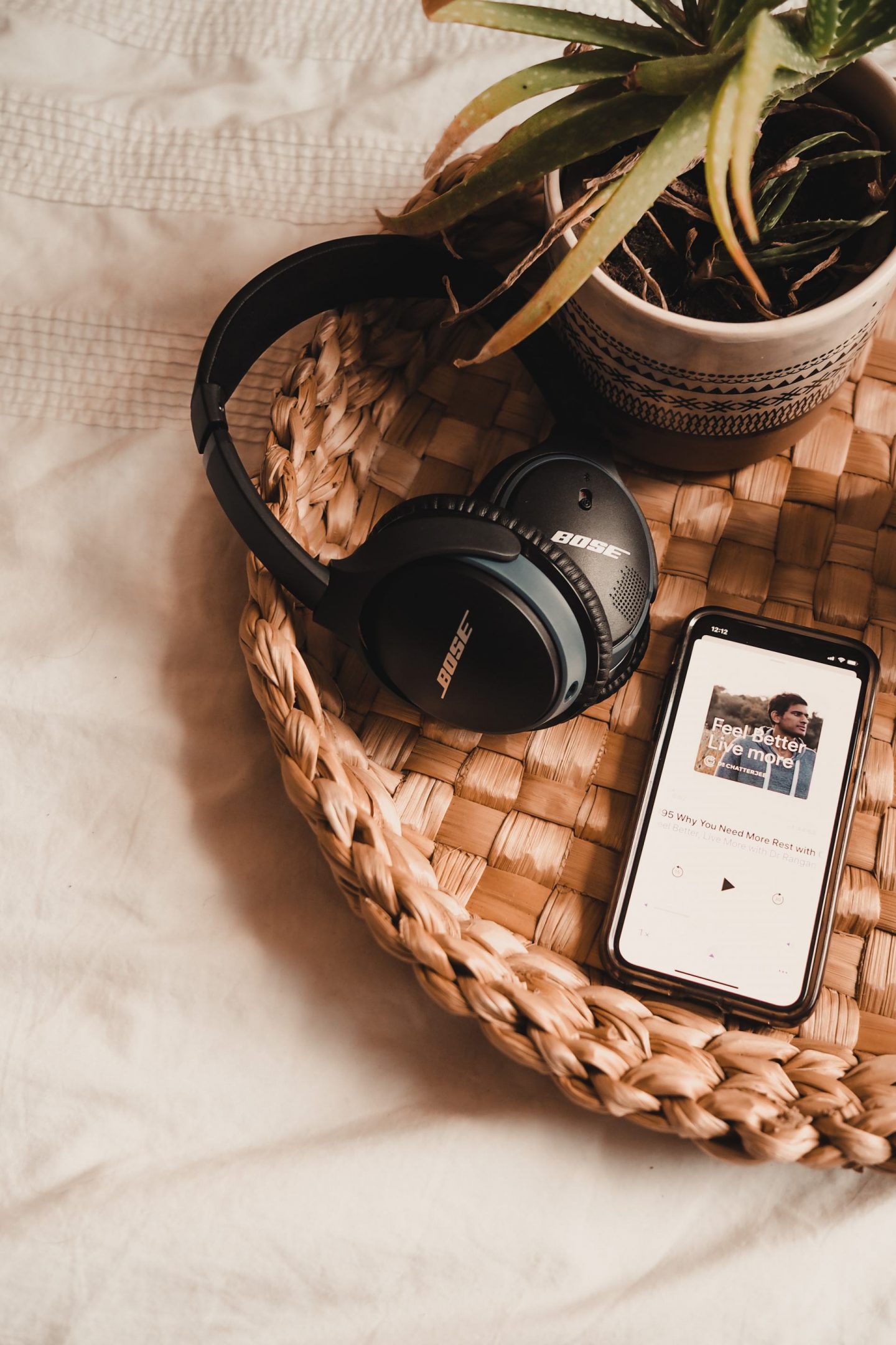 5 podcasts you need to listen to for wellbeing : iPhone and bose headphones on bamboo tray with white bedding behind